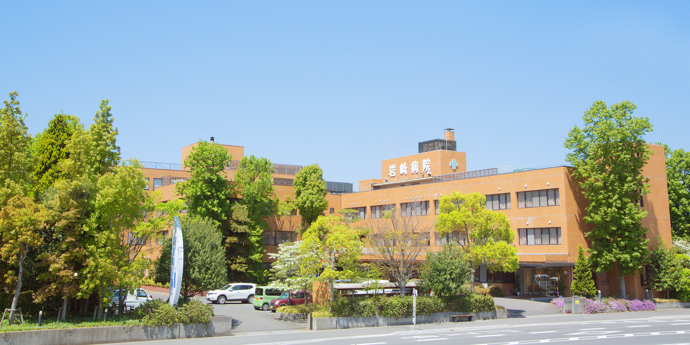 介護施設の建物外観。レンガ造りの温かみある多階建て施設。駐車場と緑に囲まれている。