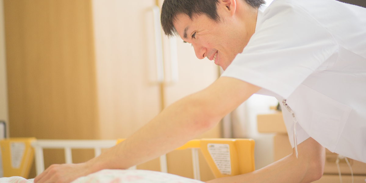 職員が居室で入居者の世話をしている様子。ベッド周辺での介護業務。